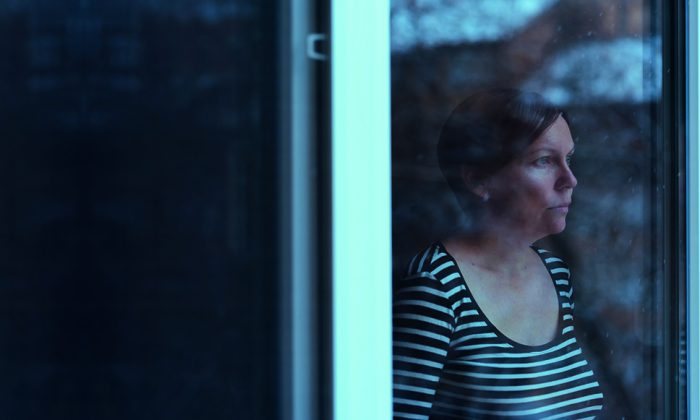 Depressed woman standing by the window and looking outside