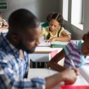 African american young male teacher assisting african american elementary girl studying at desk. unaltered, education, childhood, teaching, assistance, studying and school concept.