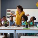 Surprised caucasian female teacher looking at african american elementary students at desk in class. unaltered, education, environment, teaching, sustainable lifestyle and school concept.