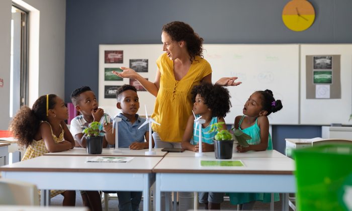 Surprised caucasian female teacher looking at african american elementary students at desk in class. unaltered, education, environment, teaching, sustainable lifestyle and school concept.