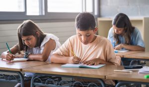 Hispanic,Primary,School,Boy,And,Girls,Writing,Test,At,Desk