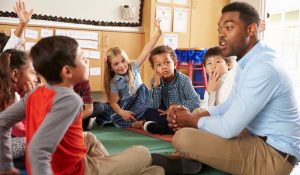 Elementary,School,Kids,And,Teacher,Sit,Cross,Legged,On,Floor