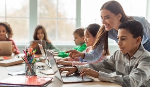 Teacher,Teaching,Diverse,School,Kids,Using,Laptop,In,Classroom.,African