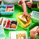 Children's,Hands,Reaching,For,Colorful,Lunchboxes,Filled,With,Sandwiches,,Fruits,