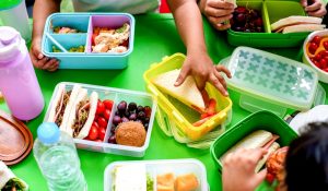 Children's,Hands,Reaching,For,Colorful,Lunchboxes,Filled,With,Sandwiches,,Fruits,