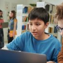 Portrait,Of,Young,Boy,Using,Laptop,In,School,Library,With
