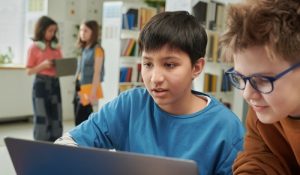 Portrait,Of,Young,Boy,Using,Laptop,In,School,Library,With