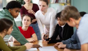 Involved,Teenage,Students,Discussing,The,Task,At,Table,While,Teacher