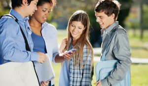 Young,Female,Student,Showing,Mobilephone,To,Classmates,In,College,Campus