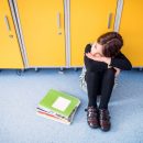 Portrait,Of,Schoolgirl,Sitting,By,Lockers.,Student,Girl,With,Bag