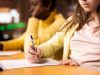 Two,Diverse,Schoolgirls,Focused,On,Writing,An,Essay,In,A