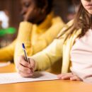 Two,Diverse,Schoolgirls,Focused,On,Writing,An,Essay,In,A