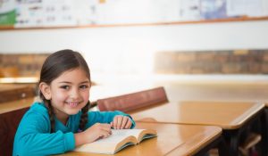 Child,Female,Student,Sitting,In,Classroom,At,Desk,Reading,Book,