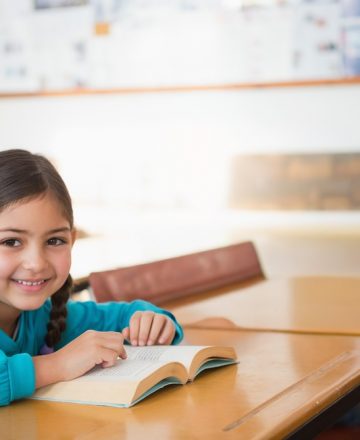 Child,Female,Student,Sitting,In,Classroom,At,Desk,Reading,Book,
