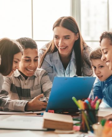 Happy,Female,Teacher,Assisting,Students,In,Classroom,,Educating,Children,,Learning