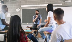 Teenager,Students,Listening,And,Talking,To,Friendly,Young,Male,Teacher