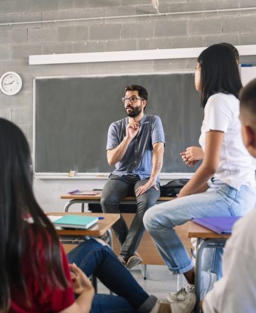 Teenager,Students,Listening,And,Talking,To,Friendly,Young,Male,Teacher